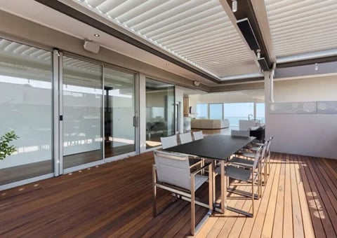 Modern rooftop deck with wooden flooring, glass sliding doors, dining table, and city views